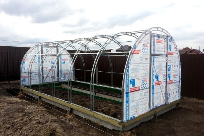 Ein schweres Gewächshaus aus Bögen mit einem Abdeckmaterial wird auf ein Streifenbetonfundament gelegt